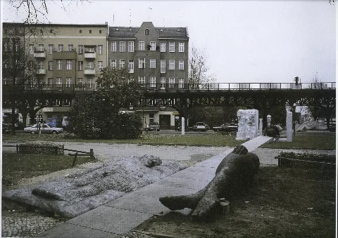 Ansicht des Skulpturen-Ensembles „Menschenlandschaft Berlin“ entlang des Wegbandes, aufgenommen von der Schlesischen Straße in Richtung Spreeufer. Das Skulpturen-Ensemble entstand im Rahmen eines Bildhauersymposions 1987 als Beitrag des Bezirks Kreuzberg zur 750-Jahr-Feier Berlins, initiiert vom Kunstamt Kreuzberg und unterstützt von der Internationalen Bauausstellung (IBA). Der Titel soll einen Bezug zur Vergangenheit und Gegenwart des Quartiers im östlichen Kreuzberg herstellen und Berlin als weltoffenen Stadt, deren sozialer und kultureller Reichtum durch Menschen aus aller Welt entstanden sei, präsentieren. Acht internationale Bildhauer*innen – Schang Hutter (Entwurfsphase), Louis Niebuhr, Rudolf Valenta, Andreas Frömberg, Azade Köker, Mehmet Aksoy, Leslie Robbins und Andreas Wegner – schufen Arbeiten für das Ensemble. Finanziert wurde das Projekt aus dem Senatsfonds „Kunst im Stadtraum“. Sammlung FHXB Friedrichshain-Kreuzberg Museum