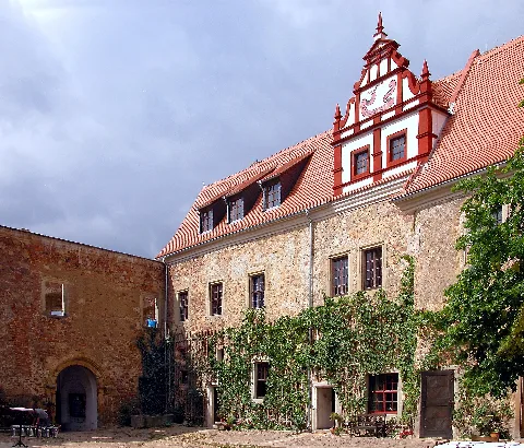 23.08.2003 01665 Scharfenberg (Klipphausen), Schloßweg 1: Schloß (GMP: 51.125283,13.527484). 1227 erste urkundliche Erwähnung, ist aus einer Burg der Bischöfe von Meißen hervorgegangen. Im 16. Jahrhundert Erbauung eines Renaissanceschlosses. 1618-1648 im 30 jährigen Krieg zerstört. 1654 Bau des heutigen Schlosses durch Haubold von Miltitz. Am 22. Oktober 1940 verkaufte Carl Freiherr von Miltitz das Schloß an Johann Heinrich Reichel aus Berlin-Neukölln. Da zum Schloß keine landwirtschaftlichen Flächen mehr gehörten, wurde der Besitz 1945 nicht enteignet. Allerdings wurde das Schloß von der Gemeinde Scharfenberg verwaltet und zur Unterbringung von Flüchtlingen genutzt. Aufgrund mangelnden Bauunterhalts setzte der Verfall ein. In den 1980er Jahren zogen Künstler und junge Leute aus der alternativen Szene in das Schloß, die in freiwilligen Arbeitseinsätzen versuchten, die zerfallenden Schloßbauten zu retten. 1997 verkauften Reichels Erben das Schloß an den Kunsthändler Gert Lippold, der das Schloß als Wohnsitz für sich und seine Familie, als Veranstaltungszentrum und als Hotel ausbaute. Schloßhof nach Südwesten mit innerem Burgtor im Südflügel und der Ostfassade des Westflügels. [DSCN]20030823200DR.JPG(c)Blobelt