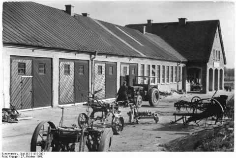 For documentary purposes the German Federal Archive often retained the original image captions, which may be erroneous, biased, obsolete or politically extreme. Groß-Hennersdorf, Blick auf den Hof der MTS Zentralbild Krueger He-Bed. 27.10.1953 MTS Groß-Hennersdorf - kulturelle und technische Basis des Dorfes Der Freund und Helfer aller werktätigen Einzelbauern und Genossenschaftsbauern in Groß-Hennersdorf, Kreis Löbau Bez. Dresden ist die MTS Groß-Hennersdorf. Die 97 Traktoristen der MTS bearbeiten eine landwirtschaftliche Nutzfläche von 10.000 ha und führen die Feldarbeiten im Zweischichtensystem durch. Bis zum Jahresende will die MTS ihr Jahressoll mit 120% übererfüllen. Diese Verpflichtung ist ein Dank für die großen finanziellen Mittel, die unsere Regierung zum Bau von kulturellen und sanitären Einrichtungen, sowie zum Bau von Traktorengaragen und Wohnungen für Traktoristen der MTS Groß-Hennersdorf zur Verfügung stellte. UBz: Für 16 Traktoren wurden neue Garagen auf der MTS Groß-Hennersdorf gebaut. (Ganz rechts) Das Verwaltungsgebäude der MTS.