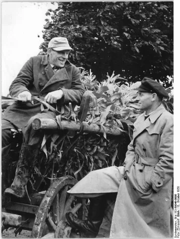 For documentary purposes the German Federal Archive often retained the original image captions, which may be erroneous, biased, obsolete or politically extreme. Zurow, Maisernte, Bauern im Gespräch Zentralbild Zühlsdorf Mellahn Zü-Noa 10.10.1958 Plane mit - arbeite mit - regiere mit. Die Gemeinde Zurow, Kreis Wismar, kann auf eine erfolgreiche Zusammenarbeit ihrer Volksvertretung, den Ausschüssen der Nationalen Front und den Bewohnern zurückblicken. Das konnte Prof. Albert Norden in seinem Referat auf dem III. Kongress der Nationalen Front berichten. In dieser Gemeinde fand vor Annahme eine gründliche Aussprache in den Hof- und Hausgemeinschaften der LPG und allen MTS über den Perspektivplan der Gemeinde statt. Der Plan wurde auch von allen Einzelbauern und 5 weiteren Mitglieder konnten für den Eintritt in die LPG gewonnen werden. UBz: Der Bürgermeister Fritz Knöppke (rechts) im Gespräch mit dem werktätigen Einzelbauern Walter Hensel. Walter Hensel tritt am 1.1.1959 der LPG "Fortschritt"" bei. Er wird 9 Hektar Land, 5 Milchkühe, 1 Stärke, 1 Kalb, 10 Schweine, 2 Pferde und 2 Schafe in die LPG einbringen. Walter Hensel war zweimal Sieger im Wettbewerb für die tierische Produktion. Er sagt; ""Durch gemeinsames Wirtschaften erreichen wir schneller den Sieg des Sozialismus.