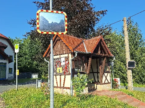 Oberndorf Wendeschleife bus stop in the Oberndorf district of the municipality of Kraftsdorf, Greiz district, Thuringia, Germany. The photograph shows the half-timbered bus shelter with a notice board, as well as a traffic mirror and the bus stop sign.