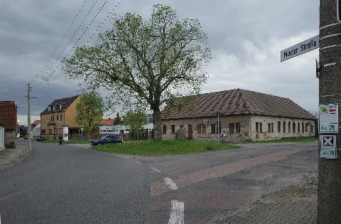 Dessau-Roßlau, Ortsteil Törten. Möster Straße mit der ehemaligen Gaststätte Spahrs, der leerstehenden Grundschule und dem Kriegerdenkmal. Die Wegweiser zeigen die Wegführung vom Fernwanderweg E11, Gartenreichtour Fürst-Franz und der Rundtour Dessau-Roßlau.