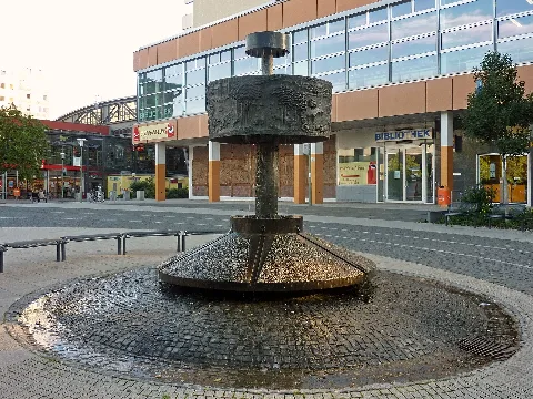 Nordseite des Fontanebrunnens am Rand des Heinrich-Dathe-Platzes in Berlin-Friedrichsfelde. Der Brunnen mit bronzenem Reliefring wurde im Jahr 1982 nach einem Entwurf von Hans-Detlef Hennig gefertigt und die ursprüngliche Basisanlage eines kreisförmigen Hauptbeckens aus Beton im Jahr 2009 neu gestaltet.