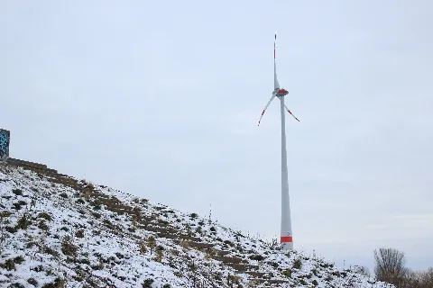 Künstlicher Erdhügel mit Treppenaufstieg im Schnee im Stadtrandpark Neue Wiesen in der Stadtrandsiedlung Malchow im Berliner Bezirk Pankow. Im Hintergrund steht eine Windkraftanlage.