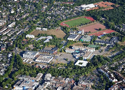Meckenheim, Neue Mitte mit Rathaus, Jungholzhalle, Hallenbad, LVR-Klinik, Schulcampus und Sportstätten. Rechts hinter dem Hallenbad die Anlage des Modell-Auto-Clubs Meckenheim e.V. Links: Siebengebirgsring, unten Königsberger Straße, darunter Fußgängerzone „Neuer Markt“. Luftaufnahme 2022, Blick aus nordwestlicher Richtung