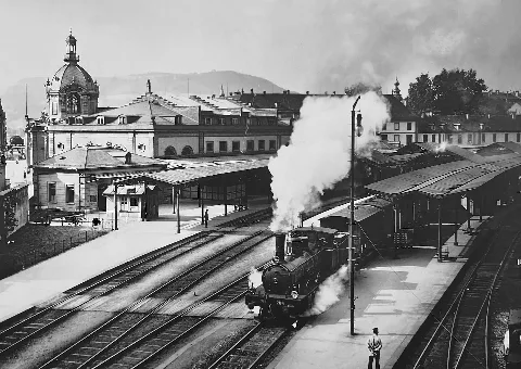 Neuer Bahnhof Bern mit dem Aufnahmegebäude aus dem Jahre 1891. Bei der abgebildeten Lokomotive handelt es sich um eine 1'C-Schlepptender Dampflokomotive der Schweizerischen Centralbahn (SCB) er B 3/4 aus der Serie 201 bis 215, von der in den Jahren 1892 bis 1896 zehn Stück von der Elsässischen Maschinenbaufabrik (SACM) in Belfort und fünf Stück von der Schweizerischen Lokomotiv- und Maschinenfabrik (SLM) in Winterthur gebaut wurden. Nach der Verstaatlichung der SCB 1902 wurden die Loks von den Schweizerischen Budnesbahnen (SBB) mit den Nummern 1471-1485 geführt und 1925 ausrangiert. Der Hauptbahnhof von Bern teilt den Vorteil unmittelbarer Zentrumslage mit dem Nachteil, zwischen der historischen Altstadt und der Grossen Schanze (mit der höher gelegenen Universität und der heutigen SBB-Generaldirektion) eingezwängt zu sein – noch dazu in einer Kurvenlage. Von Anfang an zu klein disponiert, wurde er bis in jüngste Zeit immer wieder um- und ausgebaut. An der jetzigen Lage neben der Heiliggeistkirche wurde der Bahnhof am 1 Mai 1860 eröffnet. Vorher hatte ein Provisorium auf dem Wylerfeld ausserhalb der Stadt die Züge der am 16. Juni 1857 eröffneten Bahnstrecke Herzogenbuchsee–Bern der Schweizerischen Centralbahn (SCB) und der am 1. Juli 1859 in Betrieb gegangenen Bahnstrecke Bern–Thun aufgenommen. Erweiterungspläne beschäftigten die verantwortlichen Eisenbahndirektionen und die Behörden der Stadt von Anbeginn auch am neuen Standort - erst recht, als die Bernischen Staatsbahnen 1864 eine Verbindung von Bern nach Biel/Bienne bauen wollten. Es wurden immer wieder neue Projekte vorgelegt, unter denen sowohl Kopfbahnhöfe figurierten wie die schliesslich realisierte Verlegung der Gleise zu einem Durchgangsbahnhof in einen Bogen hinter dem Bürgerspital (im Bild rechts). Dafür musste ein Teil der Grossen Schanze abgebrochen werden. Die als Kompromiss aus mehreren Konkurrenzprojekten hervorgegangene Lösung wurde erst im Jahr 1891 mit der Eröffnung des neuen Aufnahmegebäudes abge