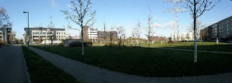Berlin-Hellersdorf, Panoramaschwenk über einen namenlosen Platz zwischen den Straßen 'Riesaer Straße' (nord-östlich), 'Mittweidaer Straße' (süd-östlich), 'Döbelner Straße' (süd-westlich) und 'Frohburger Straße' (nord-westlich). Der Schwenk fängt links mit der Döbelner Straße an, welche auch Fotostandort ist. Rechts ended er mit dem Wohnblock an der Mittweidaer Straße, welcher im Bild File:Mittweidaer Str Hellersdorf 2012-01-13 AM;A fec (36s).jpg noch kompletter zu sehen ist. Das Gebäudekarree, welches von links bis zur Bildmitte geht, ist ein Bürokomplex. In diesem befinden sich unter anderem einige staatliche Einrichtungen wie das Sozialamt, das Jugendamt und das Finanzamt von Marzahn-Hellersdorf. Dieser Park ist Teil der 'Park-Trilogie' in Hellersdorf, welche den Bereich unter den Freileitungen der Hochspannungstrasse beinhaltet. Von der Hönower Weiherkette beginnend bis an die Siedlung von Kaulsdorf heran. Hier im Park steht wie zu sehen ist, einer der Masten der Trasse an welchen die Trassenführung abknickt.