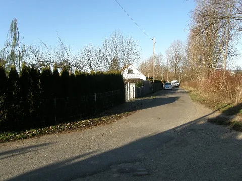 Berlin-Kaulsdorf an einen Knick der Straße „Randweg“, welche im Abschnitt voraus die Ortsgrenze zu Hellersdorf bildet, der Standort selbst liegt dabei noch in Hellersdorf. Blick westlich, leicht nördlich, das Eckgrundstück links ist die Nr. 20 und die zu sehende weiße Giebelwand gehört zur Nr. 18 vom Doppelhaus Nr. 18 und 16. Im weiteren Verlauf endet / beginnt die Straße an der Straße „Kreppfuhlweg“. Dort gibt es nach rechts auch einen Zugang in den Grünzug „Park-Trilogie“. Rechts vom Standort mündet die fußwegige Verlängerung vom Roßweiner Ring ein, über diese gelangt man zu einer kleinen Eigenheimsiedlung am Roßweiner Ring. Außerdem geht von diesem Verbindungsweg in süd-östliche Richtung ein Weg durch ein Teilstück des Grünzuges „Windschutzstreifen“ ab, über welchen man an der Straßenbahnwendeschleife vorbei zur Riesaer Straße wandeln kann. Nach links weg führt die Straße über die Straße „Schleipfuhlweg“ hinweg und geht kurz danach in die Ernst-Haeckel-Straße über.