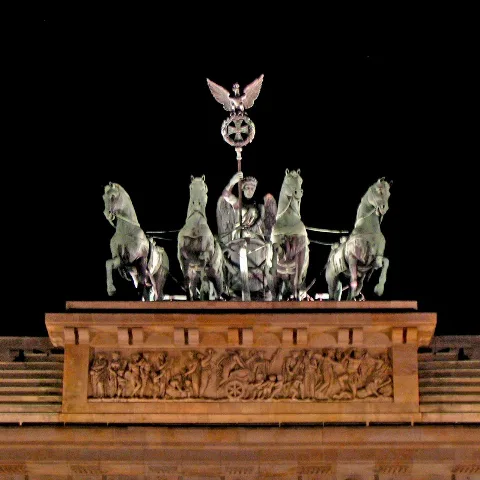 The quadriga atop the Brandenburg Gate —restored since 1991— is shining in pale-verdigris against a black backdrop of a gloomy night. In 1793, — when the so called 'French Revolutionary Wars' all over Europe were to begin —, Schadow installed in an anxious & defiant gesture towards the revolutionary Paris a peace-goddess (PAX) holding up a coronal of olive leaves behind a roman, triumphal carriage. - Under those political circumstances that build-up was obviously meant as an apotropaic allegory against the upcoming, second wave of the Great Revolution which was looming from the other side of the Rhine ... In 1806 that sculpture was of course dislodged and travelled to the Louvre by the victorious Napoléon Bonaparte but already eight years later — in 1814— the booty was tracked down and re-confiscated by the prussian General Blücher. Back in Berlin the restituted trophy was overhauled and revised by Schinkel in 1815: The once pre-reactionary Fräulein PAX (roman peace-goddess) was still turning its back against the Madame France in the West but this time she was classified into a full-blown reactionary NIKE (hellenic victory-goddess). Supporting that lurking tendency he supplemented as some new fittings the erect shaft in between the pairs of horses (“Pferdeherme”), the harness for the four domesticated mammals and the coronet of oak leaves for the goddess, and he set up the “perch”, i.e. the banner-like standard with the iron cross inside a wreath of oak leaves & acorns from which an eagle coronated by a christian cross atop a prussian crown holds lookout. The iron cross on the Brandenburg was posted in 1815 and contains the initials 'FW' and the figure '1813' in remembrance of its endowment as the prussian war decoration by Friedrich Wilhelm III. in the year 1813 which marks the beginning of the first restoration—the second such reanimation was instigated by the Hitlerists in 1933 under the pompous title “Third Reich”—of the 1806 passed away cadaver of the Holy Roma