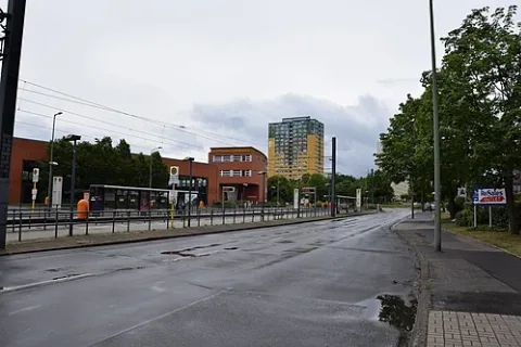 Allee der Kosmonauten in Berlin-Marzahn. Blick von der nördlichen Bushaltestelle 'Allee der Kosmonauten/Poelchaustraße', auf die gleichnamige Straßenbahnhaltestelle, das dahinter liegende 'Wilhelm-von-Siemens-Gymnasium' und das Hochhaus 'Flower-Tower' (AdK 145) hinter dem Straßenknick. Im Straßenknick ist etwas, die abgehende Poelchaustraße zu erkennen.