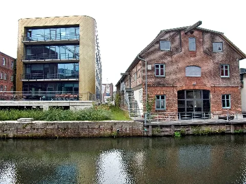 Alt und neu am Kaufhauskanal. Links die neu gebaute TU-Harburg für Luft- und Raumfahrt mit Goldfisch-Fassade, rechts daneben der alte Speicher am Kaufhauskanal, datiert erstmalig 1827. Der Speicher und weitere Gebäude sind eingetragen in der DL mit Adresse Blohmstraße 22. Hier mit Ansicht an der Wasserseite. Das Gebäude der TU-Harburg gehört nicht zum Ensemble.