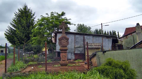 Hohes schlankes Kreuz aus rotem Sandstein mit Kruzifix aus Metall; Relief - Figuren im Sockel- und mittleren Bereich.