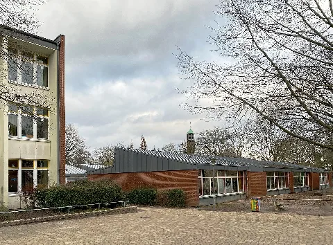 Westerschule Finkenwerder in Hamburg-Finkenwerder, Finkenwerder Landscheideweg 180, Pavillon rot (Errichtet ungefähr Ende der 1950er / Mitte der 1960er), links angeschnitten der Ostflügel des Kreuzbaus. Im Hintergrund der Glockenturm des Karmelitinnen-Klosters „Karmelzelle von der Menschwerdung“.